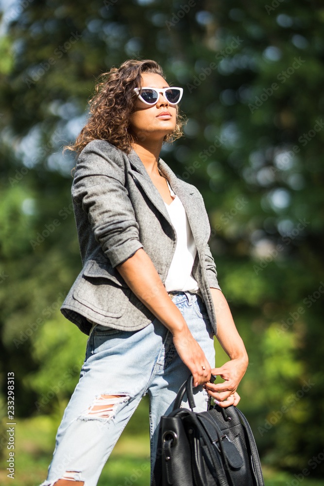 Portrait of young stylish girl walking on street, smiling and laughing on the city with backpack in the park Portrait of young stylish girl walking on street, smiling and laughing on the city with backpack in the park