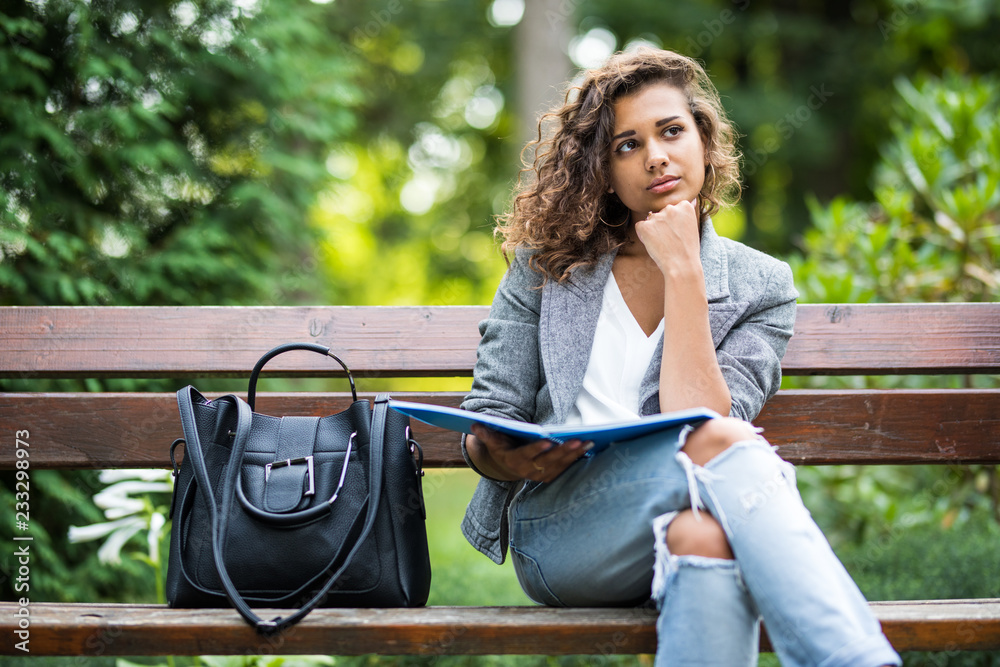 The girl sitting on a bench, reading a book in city park The girl sitting on a bench, reading a book in city park