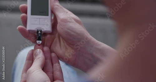 Blood sugar, diabetes and healthcare concept - a woman takes a blood sample with a lancet and measures blood sugar levels with a glucose meter at home.