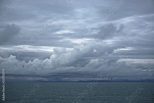 Storm clouds gathering over the deep blue waters of the Gulf of Alaska, with mountains on the coast just visible in the distance.
