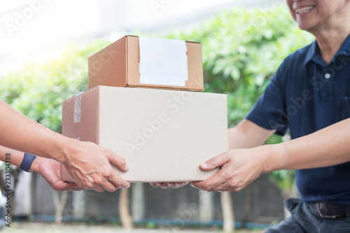 Woman receiving parcel cardboard box from delivery man Carrying Courier Shipping Mail from making an online order while standing in front of the house. © snowing12