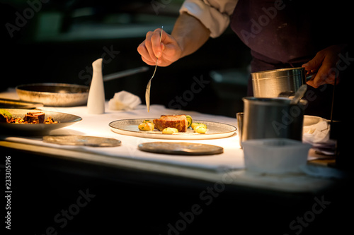 Chef preparing a plate made of meat and vegetables. The chef is pouring sauce on the plate.