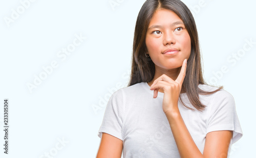 Young asian woman over isolated background with hand on chin thinking about question, pensive expression. Smiling with thoughtful face. Doubt concept. © Krakenimages.com
