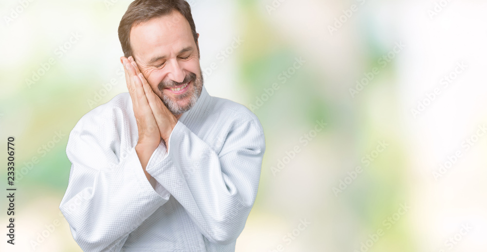 Handsome middle age senior man wearing kimono uniform over isolated background sleeping tired dreaming and posing with hands together while smiling with closed eyes. Handsome middle age senior man wearing kimono uniform over isolated background sleeping tired dreaming and posing with hands together while smiling with closed eyes.