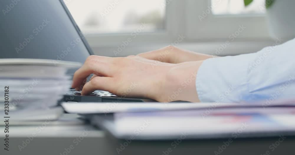Female accountant in her workplace, typing on laptop and reading a document with charts. Female accountant in her workplace, typing on laptop and reading a document with charts.