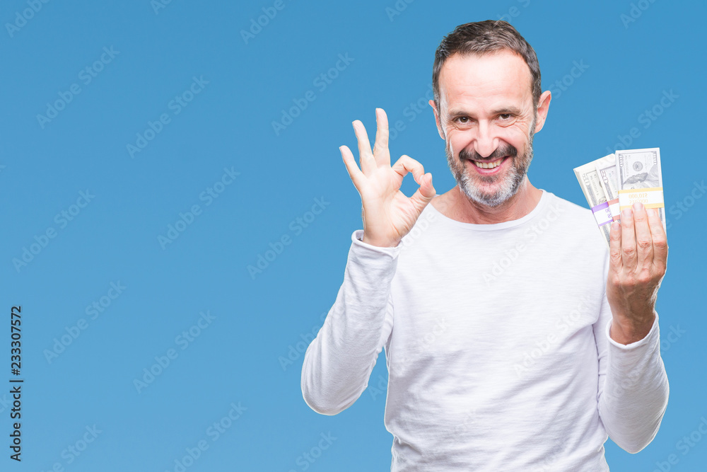 Senior hoary man holding buch of dollars over isolated background doing ok sign with fingers, excellent symbol Senior hoary man holding buch of dollars over isolated background doing ok sign with fingers, excellent symbol