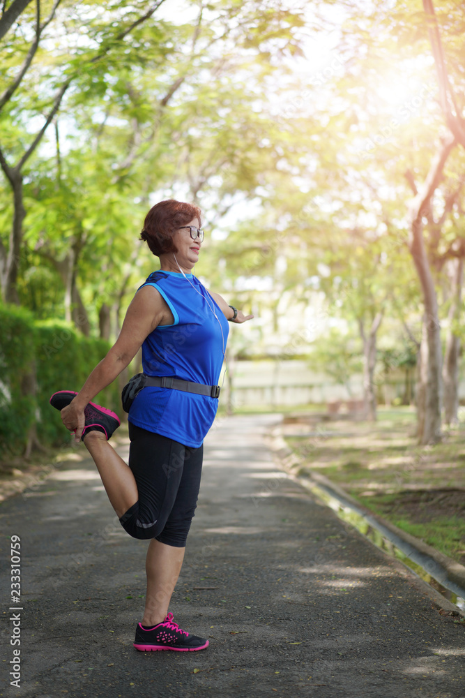 Senior asian woman stretch muscles at park and listening to music. Athletic senior exercising together outdoor. Fit senior runners stretching before running outdoors