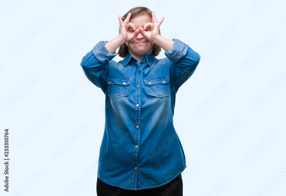 Fototapeta premium Young adult woman with down syndrome over isolated background doing ok gesture like binoculars sticking tongue out, eyes looking through fingers. Crazy expression.
