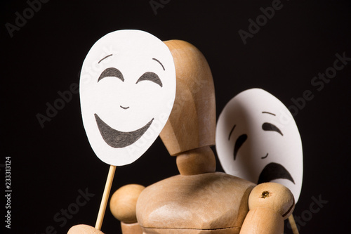 Wooden doll on hinges holds a mask in hands and covers her face on a black background