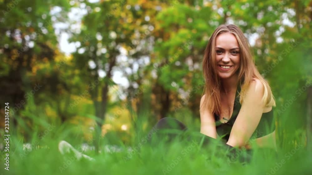 Beautiful girl sitting on the grass and stretches to his feet. Athlete doing stretching. The blonde looks at the camera and smiles. Cute girl goes in for sports in the nature. Beautiful girl sitting on the grass and stretches to his feet. Athlete doing stretching. The blonde looks at the camera and smiles. Cute girl goes in for sports in the nature.