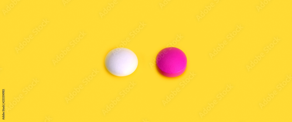 Two pills pink and white on a yellow background. View from above.