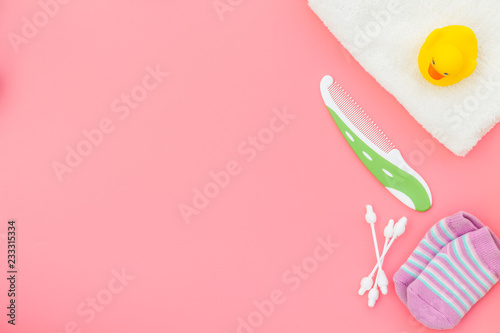 Baby care. Bath cosmetics and accessories for child with towel and yellow rubber duck on pink background top view copy space