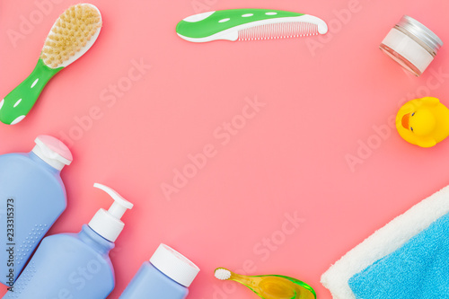 Baby care. Bath cosmetics and accessories for child. Shampoo, gel, cream, yellow rubber duck on pink background top view frame copy space