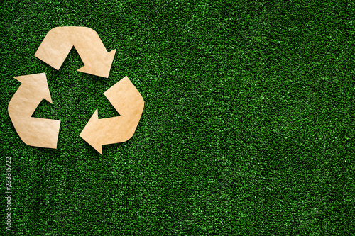 Eco recycle sign made of craft paper on green grass background top view copy space