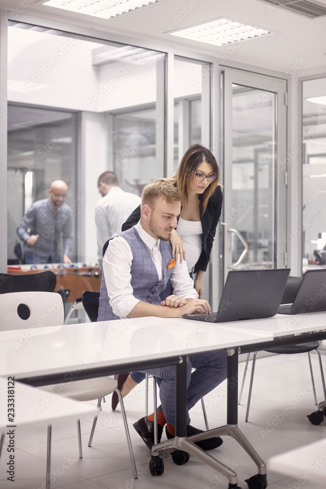 group of people, working together on laptop, some relaxing playing table football, indoors modern office building.