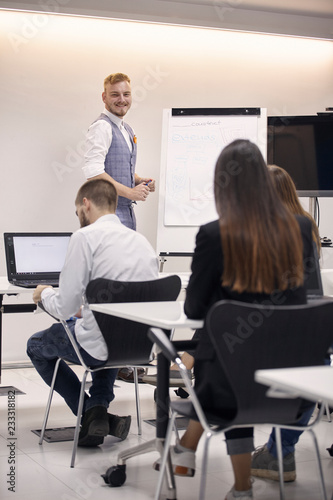 one young man smiling, 20-29 years old, presenting to group of people,  in office indoors.