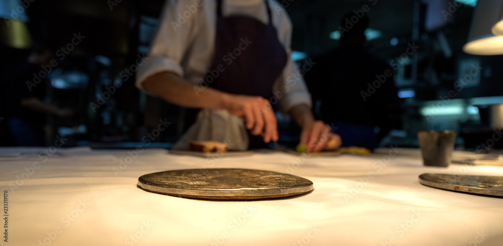 Metal plate on a white table cloth with the chef in the background. Metal plate on a white table cloth with the chef in the background.