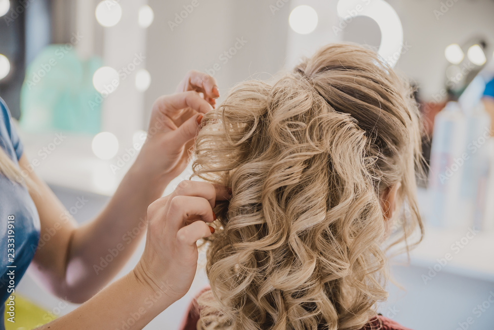 Naklejka premium female hairdresser does hair blonde girl in a beauty salon, the process of creating hairstyles