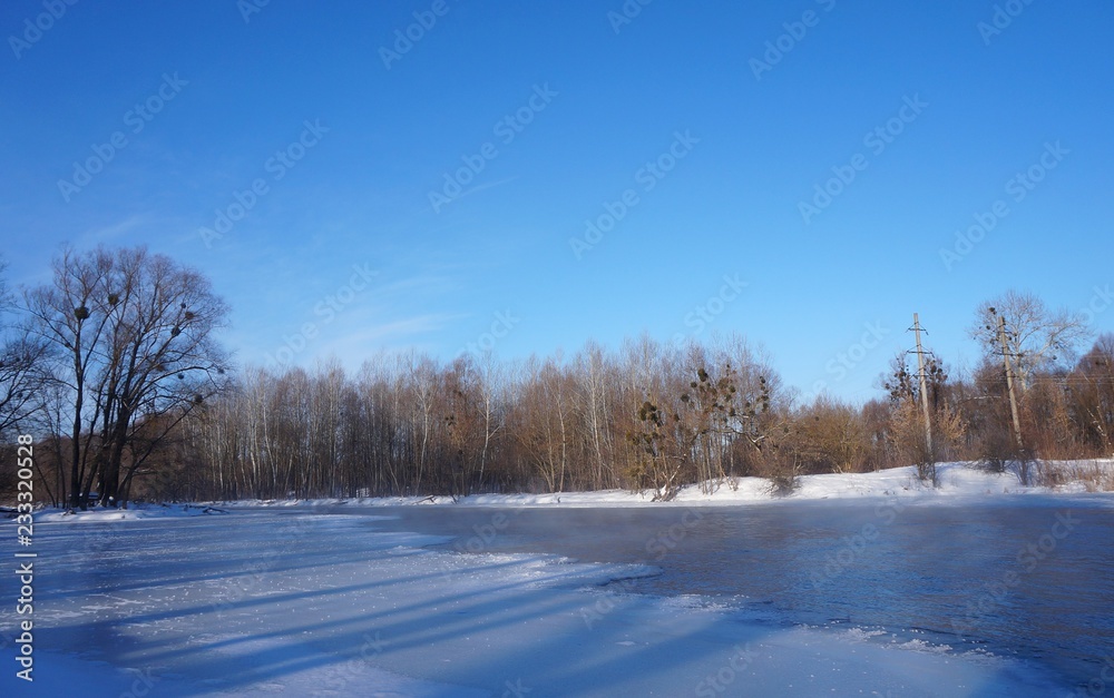 Winter Christmas landscape in pink tones,with calm winter river, surrounded by trees.Winter forest on the river at sunset. Landscape with snowy trees, beautiful frozen river with reflection in water