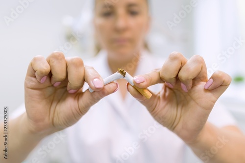 Doctor dentist breaks a cigarette, broken cigarette close up, background dental office. Stop Smoking