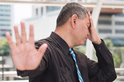 tired business man saying no. portrait of exhausted, tired asian businessman showing stop, halt hand gesture headache. 50s old southeast asian man model