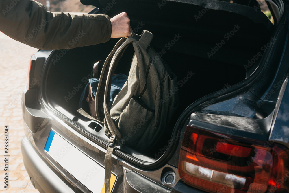 A man or a tourist puts a backpack in the trunk of a car. Preparation for the trip. The concept of tourism or travel by car. A man or a tourist puts a backpack in the trunk of a car. Preparation for the trip. The concept of tourism or travel by car.