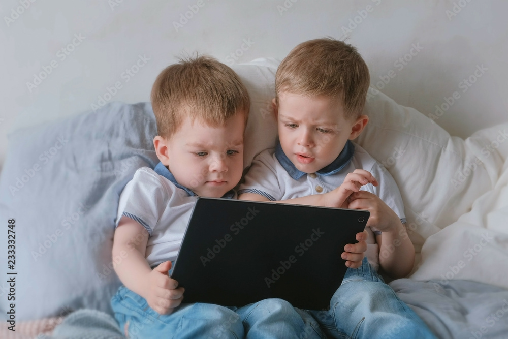 Kids with tablet. Two boys twins toddlers looking cartoon at tablet lying on the bed. Kids with tablet. Two boys twins toddlers looking cartoon at tablet lying on the bed.