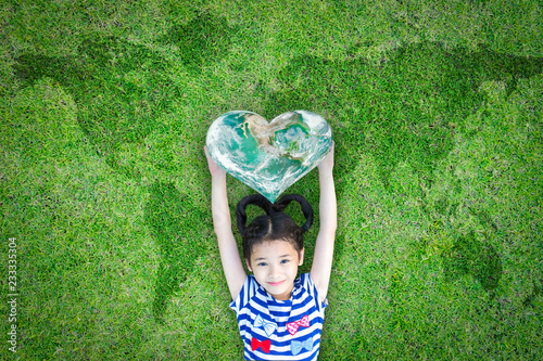 World kindness day concept with happy kid raising heart planet on ecological friendly natural green lawn. Element of the image furnished by NASA photo