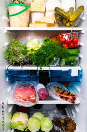 Refrigerator inside full of assorted food ingredients, vegetables, meat and dairy products photo