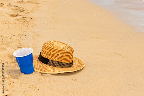 Plastic cup and hat on the beach sands as vacation concept.