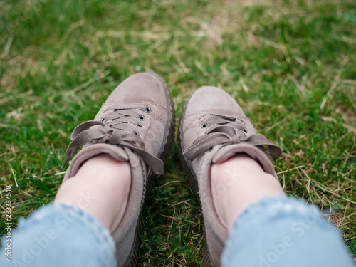Young woman, wearing in blue jeans and sneakers, sitting on the green grass, close up