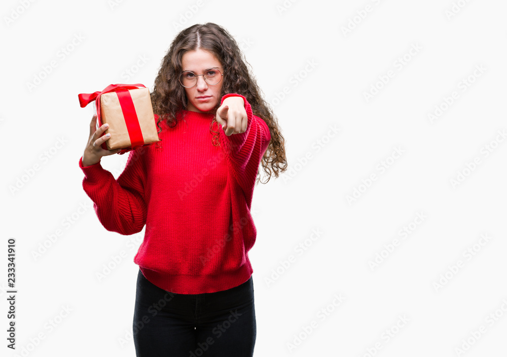 Young brunette girl holding a gift over isolated background pointing with finger to the camera and to you, hand sign, positive and confident gesture from the front Young brunette girl holding a gift over isolated background pointing with finger to the camera and to you, hand sign, positive and confident gesture from the front