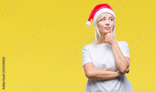 Young beautiful blonde woman wearing christmas hat over isolated background with hand on chin thinking about question, pensive expression. Smiling with thoughtful face. Doubt concept. © Krakenimages.com