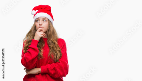 Young blonde woman wearing santa claus hat serious face thinking about question, very confused idea