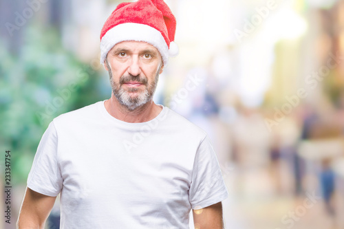 Middle age hoary senior man wearing christmas hat over isolated background with serious expression on face. Simple and natural looking at the camera.