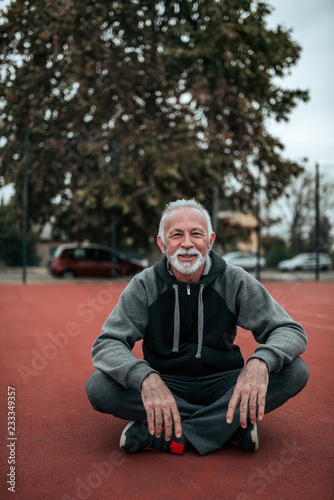 Portrait of a senior sportsman sitting on the tartan track, looking at camera. © bnenin