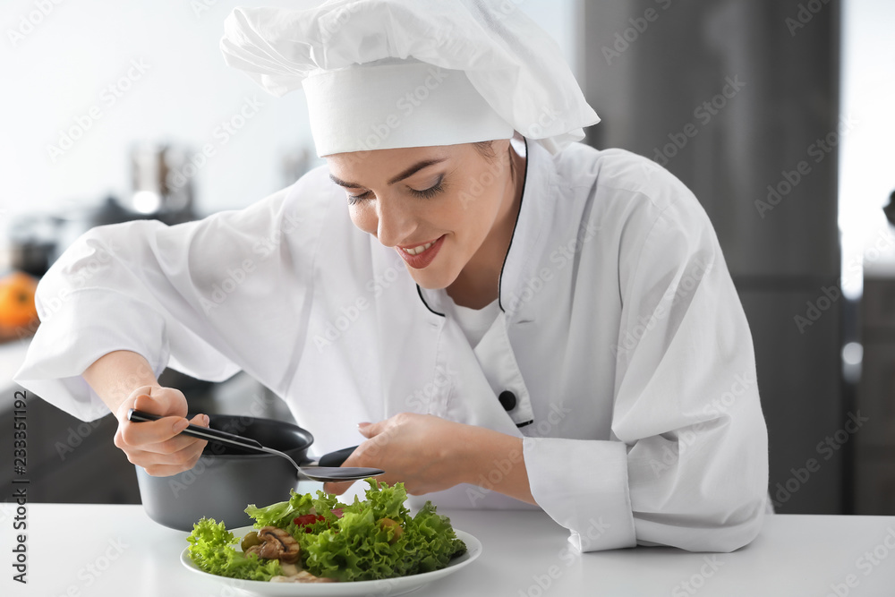 Young female chef dressing tasty salad in kitchen Young female chef dressing tasty salad in kitchen
