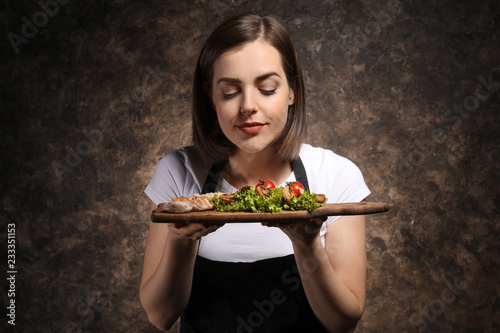 Young female chef with tasty dish on dark background