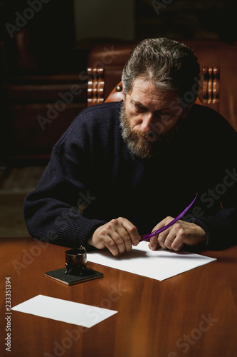 writer with beard writes on white sheet with goose feather