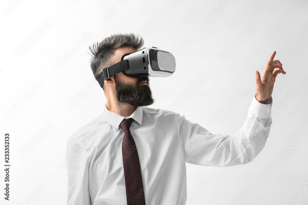 Businessman wearing virtual reality glasses on light background