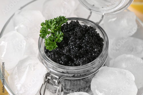Jar with delicious black caviar and ice cubes in bowl, closeup