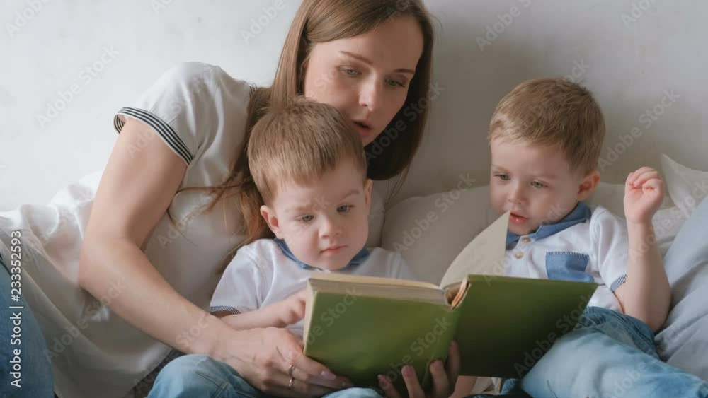 Family mom and two twin brothers toddlers read books laying on the bed. Family reading time. Family mom and two twin brothers toddlers read books laying on the bed. Family reading time.