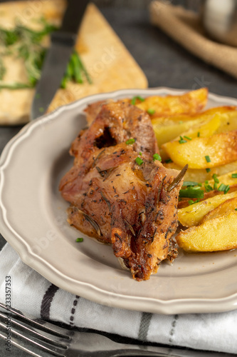 Roast pork with herbs and vegetables on rustic wooden table.