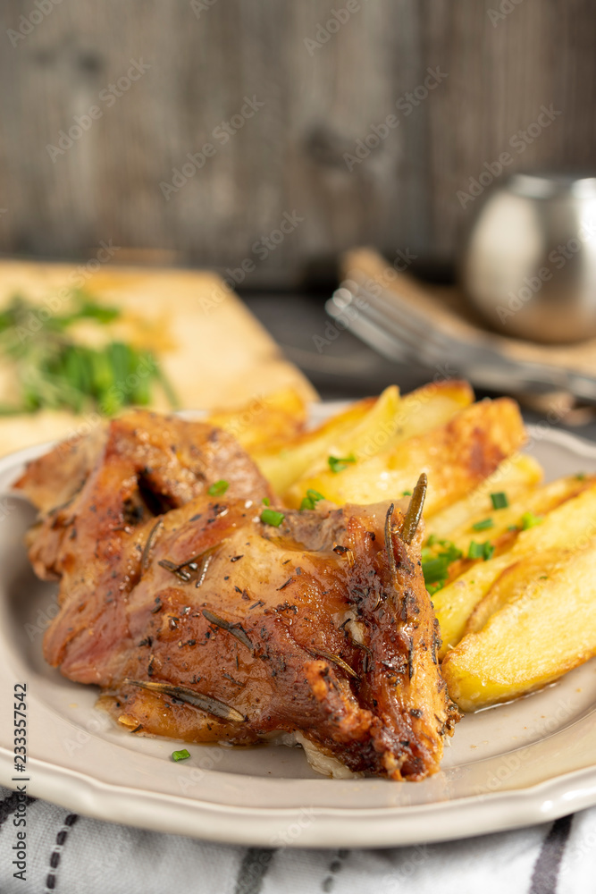 Roast pork with herbs and vegetables on rustic wooden table.