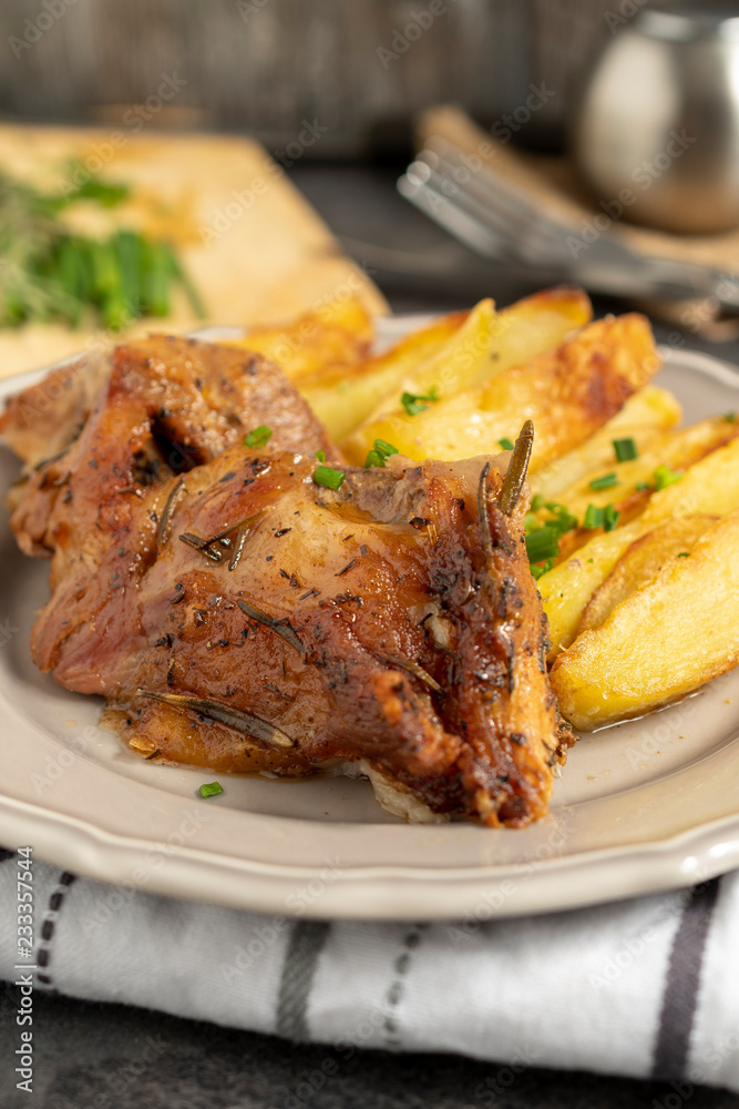 Roast pork with herbs and vegetables on rustic wooden table.