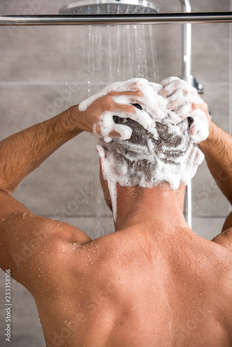 rear view of man washing hair with shampoo and taking shower