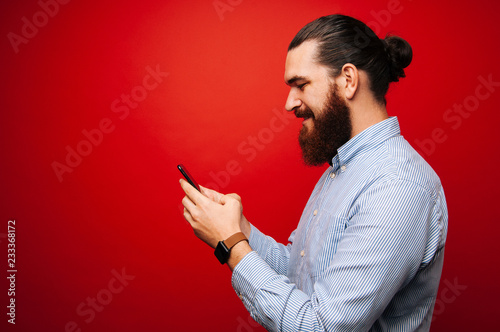 Happy man with beard texting in a mobile phone over red background