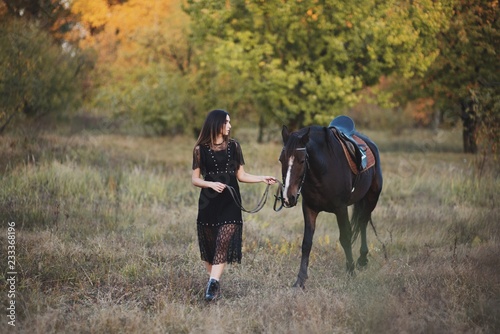 Adorable young woman walking with her horse in autumn forest