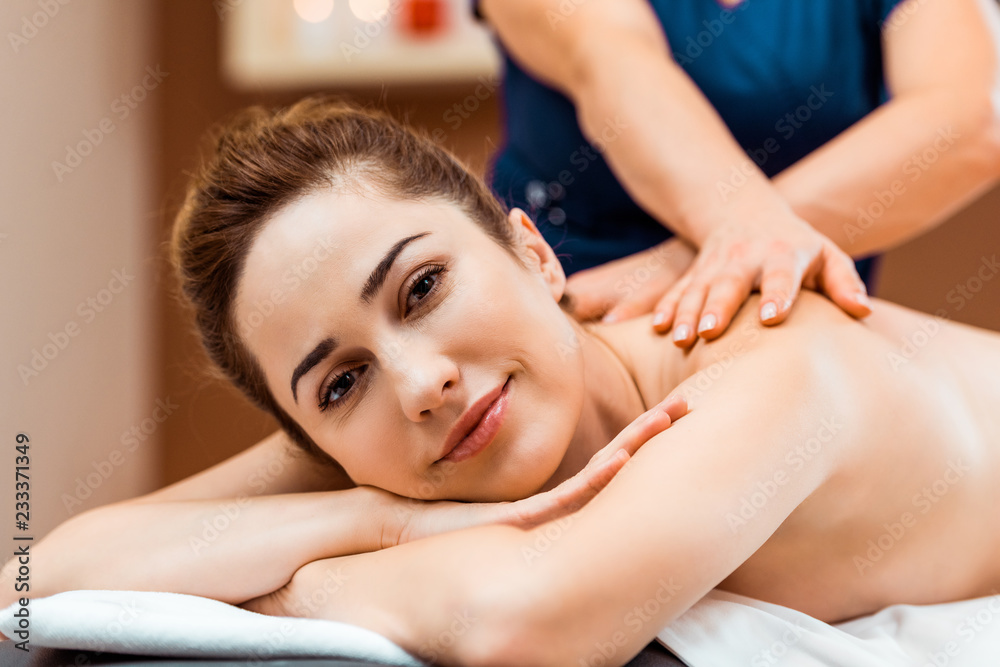 Obraz premium attractive young woman smiling at camera while having massage in spa