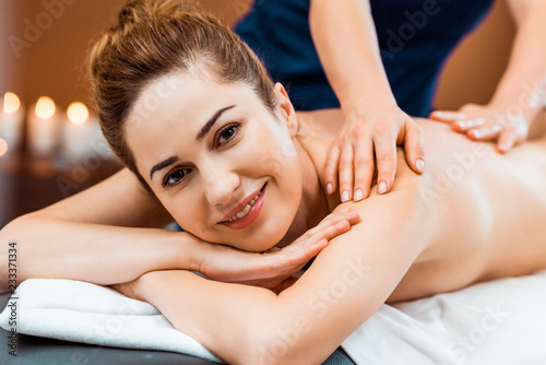 beautiful happy young woman smiling at camera while having massage in spa